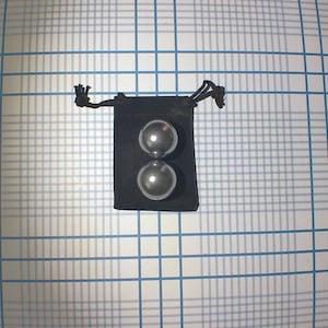 May include: Two silver metal balls in a black velvet pouch with a drawstring closure.