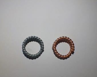 May include: Two rings with a braided rope design. One ring is silver-colored, and the other is copper-colored. The rings are circular and sit on a white surface. These rings are suitable for everyday wear.
