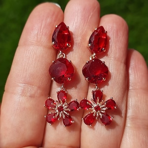 Op de afbeelding: Een paar oorhangers met rode kristallen bloemen en traanvormige stenen.