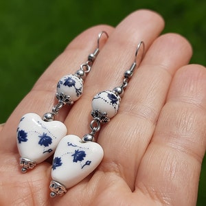 May include: A pair of dangle earrings with white heart-shaped ceramic beads with blue floral designs and silver accents.