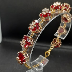 May include: Gold bracelet with red heart-shaped charms and clear crystal accents. Each charm features a flower design.