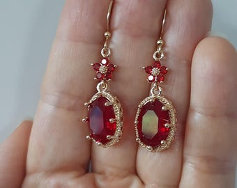 May include: A pair of gold dangle earrings with red oval-shaped stones and red flower accents.