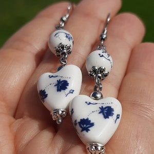 May include: A pair of dangle earrings with white heart-shaped ceramic beads with blue floral designs and silver accents.