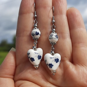 May include: A pair of silver earrings with white ceramic heart-shaped charms. The charms have a blue floral design.
