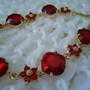 May include: A gold bracelet with red gemstone accents and small flower charms. The bracelet has an adjustable sliding clasp.