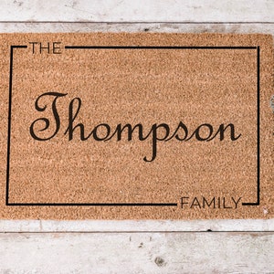 May include: A brown coir doormat with a black frame and the text "THE Thompson FAMILY" in a cursive font.