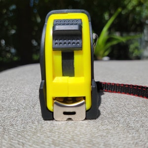 May include: A yellow and black tape measure with a red and black strap. The tape measure has a metal hook and a button to lock the tape.