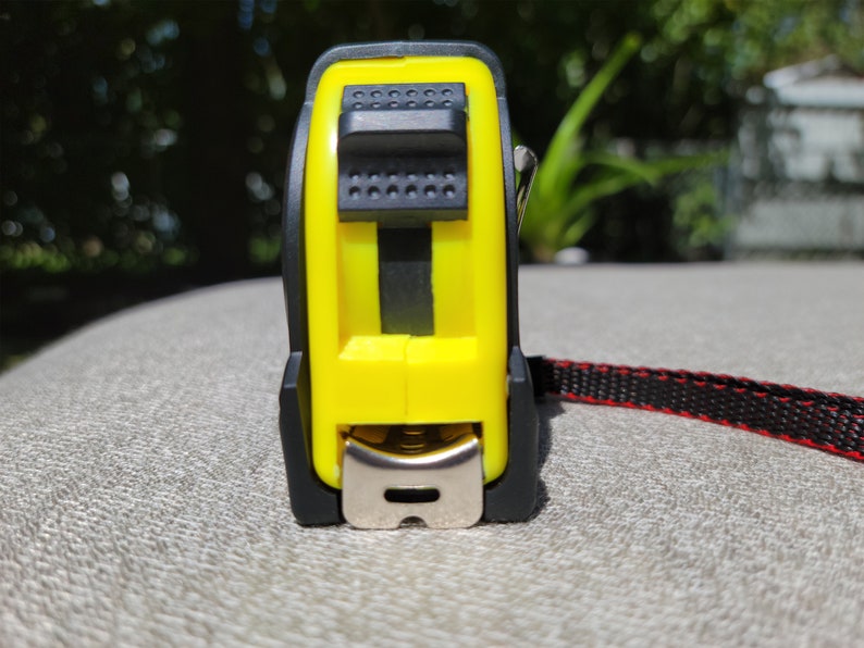 May include: A yellow and black tape measure with a red and black strap. The tape measure has a metal hook and a button to lock the tape.