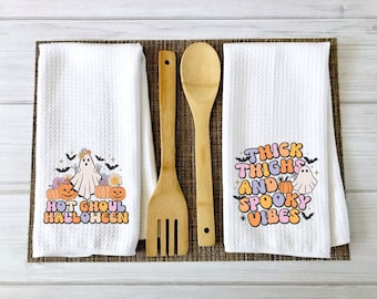 May include: Two white kitchen towels with a Halloween theme. One towel features a ghost with a flower crown and the text "Hot Ghoul Halloween". The other towel features a ghost and the text "Thick Thighs and Spooky Vibes".