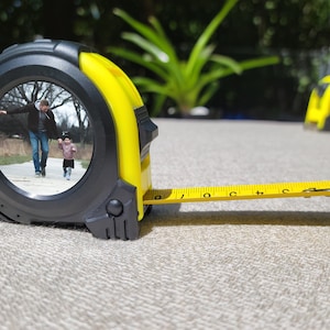 May include: A yellow measuring tape with a black case. The case has a clear window that shows a photo of a father and child walking in a park.