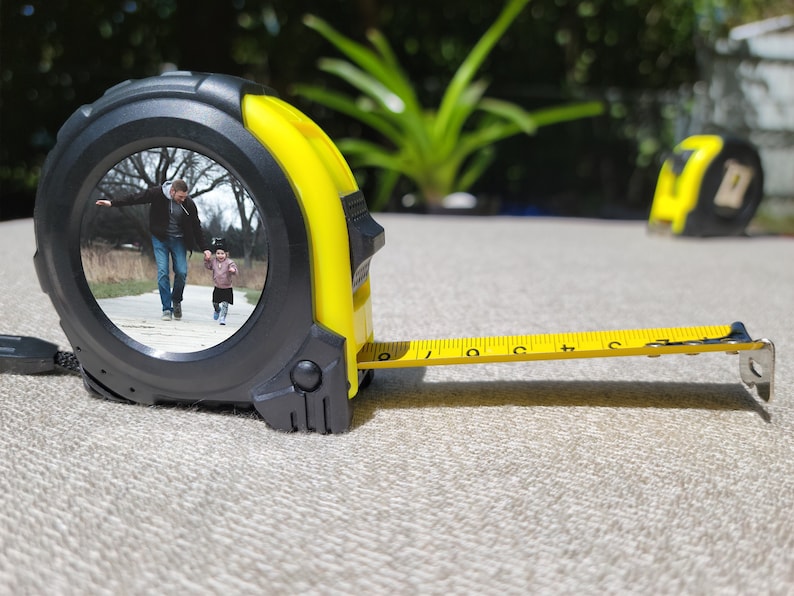 May include: A yellow measuring tape with a black case. The case has a clear window that shows a photo of a father and child walking in a park.