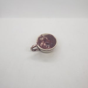 May include: A small, handmade ceramic teacup with a handle. The interior is a deep burgundy color with a speckled pattern, while the exterior is a creamy white. The cup is designed for hot beverages.