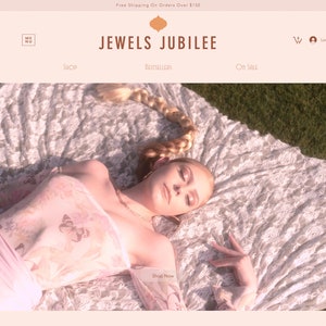 May include: A woman wearing a sheer pink floral print top with butterfly designs, lying on a white lace blanket. The blanket is on a green grassy surface. The image has a vintage, soft-focus aesthetic.