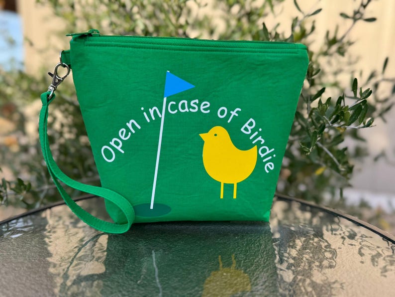 May include: Green zippered pouch with a white graphic of a golf flag and a yellow bird with the text "Open in case of Birdie".