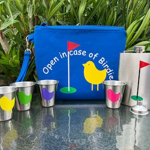 May include: A blue golf-themed pouch with the text "Open in case of Birdie" and a yellow bird graphic. The pouch is next to a silver flask with a red golf flag graphic. There are four small silver cups with colorful bird graphics.