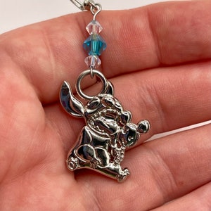 May include: Silver charm of Stitch from Lilo & Stitch, with blue and clear crystal beads hanging from a silver chain.