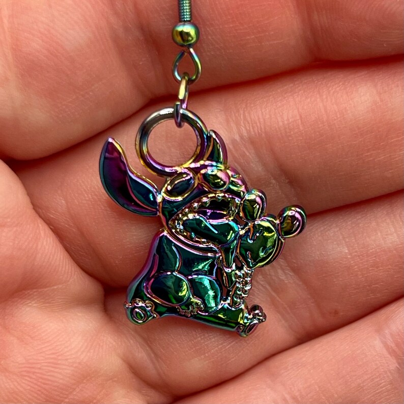 May include: Rainbow iridescent metal earring featuring a cartoon Stitch character from Lilo & Stitch. The earring is a dangle style with a small metal bead at the top.