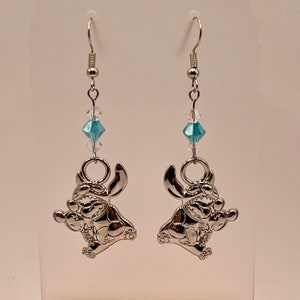 May include: Silver dangle earrings featuring a blue crystal charm and a silver Stitch character charm.