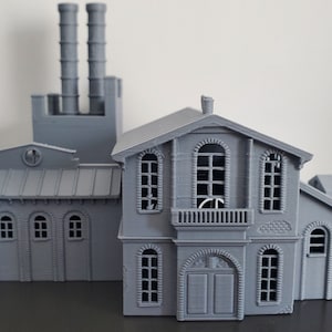 May include: A gray 3D printed model of a building with two tall chimneys and a smaller building attached to the side. The smaller building has a balcony and a door.