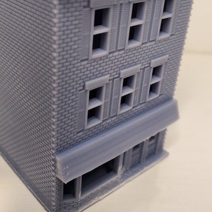 May include: A gray brick building with a storefront and multiple windows. The windows have shutters and are arranged in two rows. The building has a gray awning over the storefront.