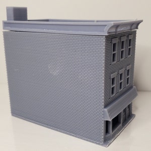 May include: A gray brick building model with a flat roof and a storefront awning. The building has three windows on each of the two upper floors.