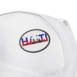 May include: White baseball cap with a black oval patch featuring the word "HAITI" in blue and red letters, with a small image of the Haitian flag inside the letters.