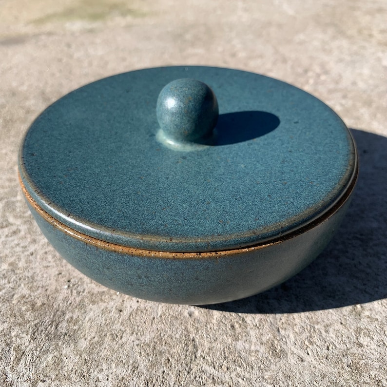 Peut inclure: Un bol en c&eacute;ramique bleu avec un couvercle. Le couvercle a un bouton rond sur le dessus. Le bol a une texture l&eacute;g&egrave;rement rugueuse.