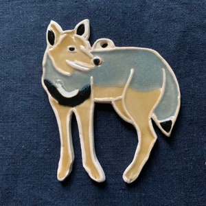 May include: A ceramic ornament of a wolf, painted in shades of blue, yellow, and black. The wolf is standing on all four legs, with its head turned to the side.