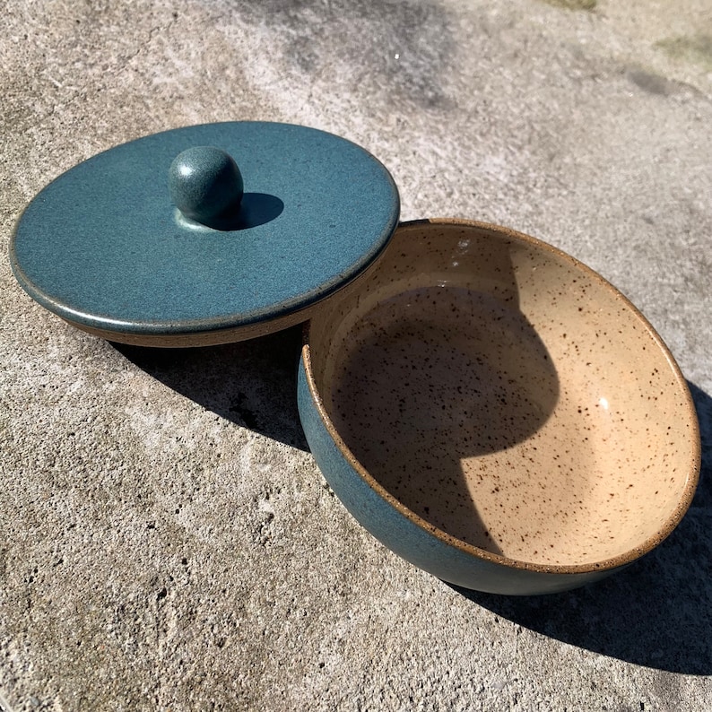 Peut inclure: Un bol en c&eacute;ramique bleu avec un int&eacute;rieur beige mouchet&eacute; et un couvercle assorti avec un bouton. Le bol et le couvercle sont tous deux &eacute;maill&eacute;s.