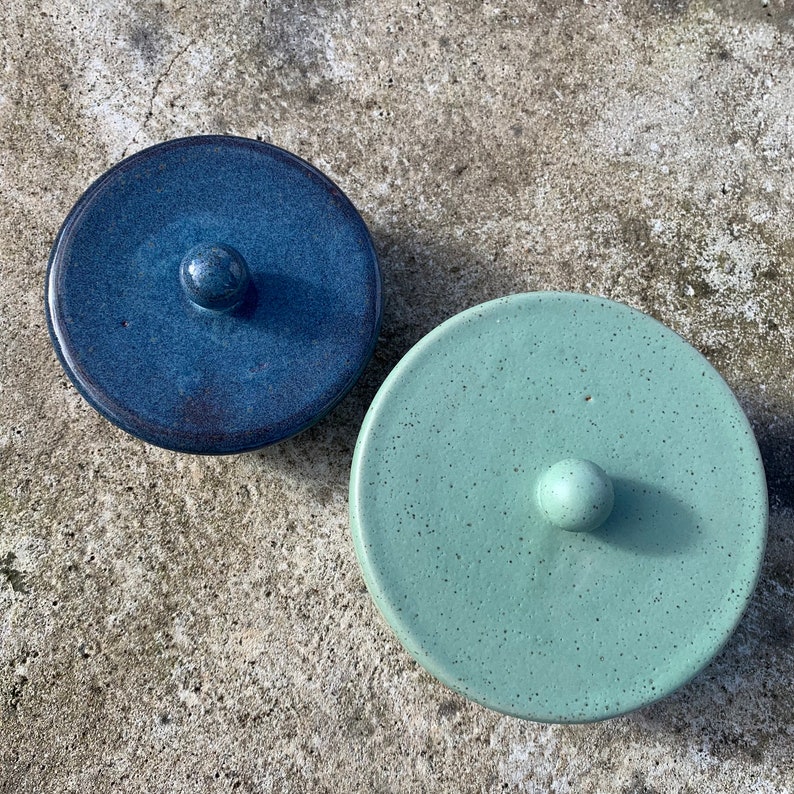 Peut inclure: Deux couvercles en c&eacute;ramique avec une finition mouchet&eacute;e. Un couvercle est bleu avec un bouton bleu fonc&eacute;, et l'autre est vert avec un bouton vert clair.
