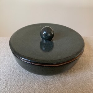 Peut inclure: Un plat en c&eacute;ramique vert fonc&eacute; avec un couvercle. Le couvercle a un bouton rond sur le dessus.