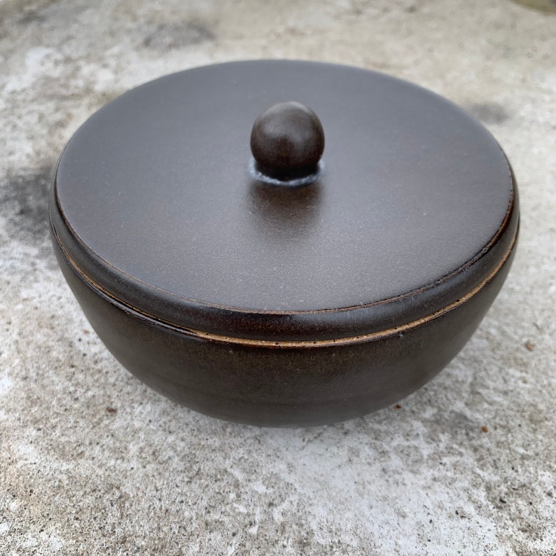 Peut inclure: Un bol en c&eacute;ramique brun fonc&eacute; avec un couvercle. Le couvercle a un petit bouton sur le dessus.