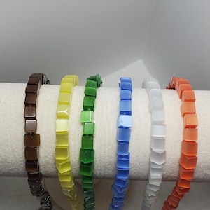 May include: A set of eight strands of square-shaped beads in various colors, including brown, yellow, green, blue, white, and orange. The beads are strung on a white surface.