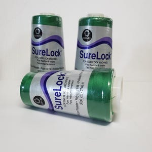 May include: Three spools of green SureLock thread for overlock machines. Each spool has a white label with purple accents and the Coats logo. The text on the label includes "Polyester File" and "3000 yds".