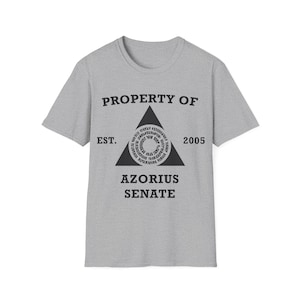 May include: A grey t-shirt featuring the text "PROPERTY OF" above a black triangle with a circular design. Below the triangle is "AZORIUS SENATE" and "EST. 2005". The shirt has short sleeves and a crew neck.