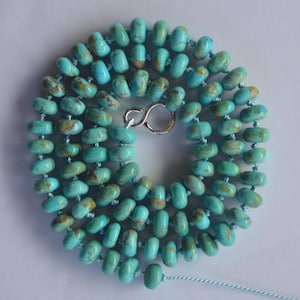May include: A turquoise bead necklace with a silver clasp. The beads are oval-shaped and have brown and tan markings. The necklace is displayed on a white surface.