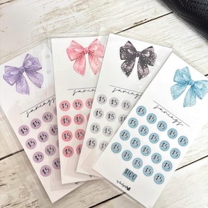 May include: Four savings tracker cards featuring bow illustrations in purple, pink, grey, and blue. Each card has circles labelled with "£5" and the word "savings" in script. One card has a "£100" label.