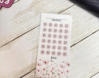 May include: A savings tracker card with the word "SAVINGS" at the top. It has pink circles with the number 10 inside, arranged in rows. The bottom features a floral and butterfly design, with the total amount of $300.