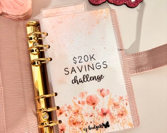 May include: A pink binder with gold rings and a clear plastic page insert with a watercolor floral design and the text "$20K SAVINGS challenge" and the logo "ez budgets" with a butterfly.