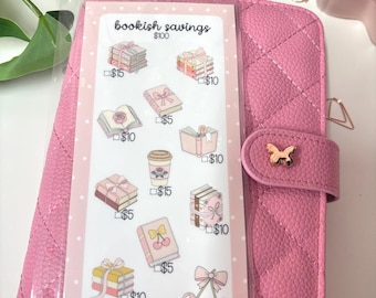 May include: Pink quilted planner with a clear pocket holding a "bookish savings" insert. The insert features illustrations of books, gifts, and a coffee cup, each with a savings amount. A gold butterfly clasp secures the planner.