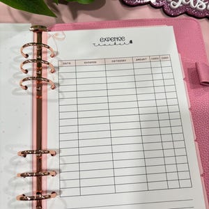 May include: Pink planner with rose gold hardware and an expense tracker insert. The expense tracker has columns for date, expense, category, amount, cash, and card. The words "expense tracker" are written at the top of the page.