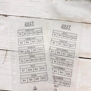 May include: Two translucent planner inserts for 2027 Fridays, featuring monthly grids with dollar amounts for January through December. Each sheet has a column of holes on the left side for binding and black printed text detailing dates and savings goals.
