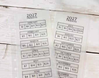 May include: Two translucent planner inserts for 2027 Fridays, featuring monthly grids with dollar amounts for January through December. Each sheet has a column of holes on the left side for binding and black printed text detailing dates and savings goals.