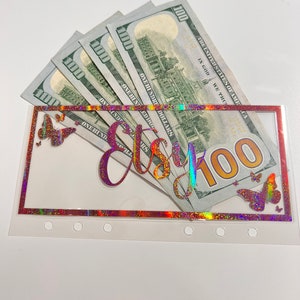 May include: A clear plastic budget envelope with the word "Etsy" in a holographic script, filled with five one-hundred dollar bills. The envelope has a holographic border and butterfly accents.