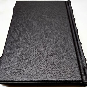 May include: A black leather-bound journal with a textured cover and a decorative spine.