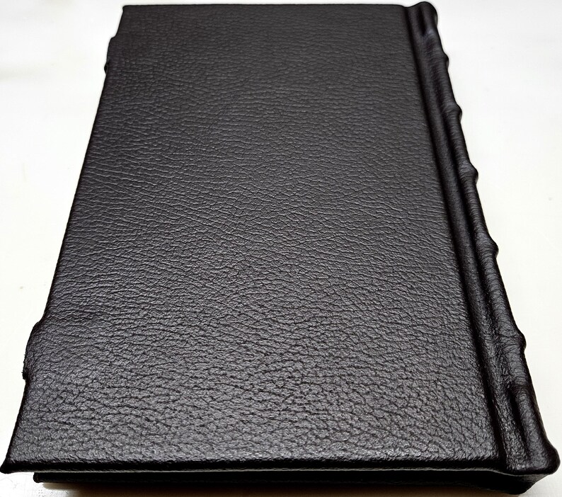May include: A black leather-bound journal with a textured cover and a decorative spine.