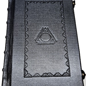May include: A black leather-bound book with a textured cover. The cover features an embossed design with a triangle and circle symbol, and decorative border. The spine has raised bands. The book is closed with a metal clasp.