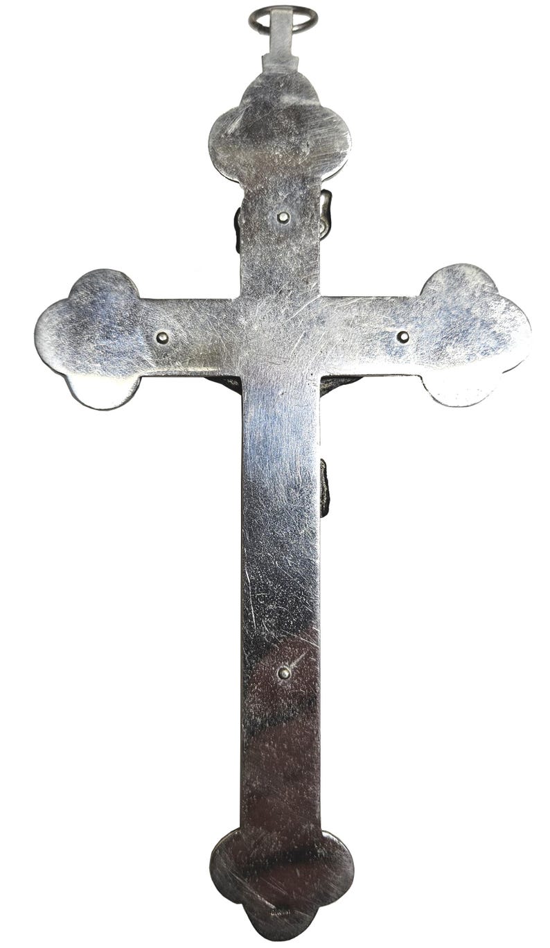 Puede incluir: Un crucifijo plateado con un dise&ntilde;o detallado. La cruz presenta bordes redondeados y una peque&ntilde;a figura de Jes&uacute;s. La parte superior tiene un lazo para colgar. El metal tiene una apariencia ligeramente envejecida.