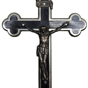Puede incluir: Un crucifijo decorativo con una cruz de madera oscura y un marco de metal plateado. La figura de Jes&uacute;s es de color bronce. La cruz tiene un lazo en la parte superior para colgar.