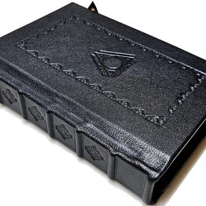 May include: A black leather-bound journal with embossed geometric designs and a triangular emblem on the cover. The spine features decorative panels. The journal has a textured surface and is closed with a small clasp.